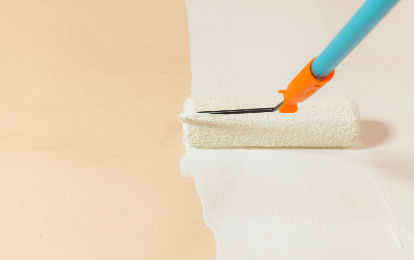 Painting a peach-coloured wall white with a roller brush