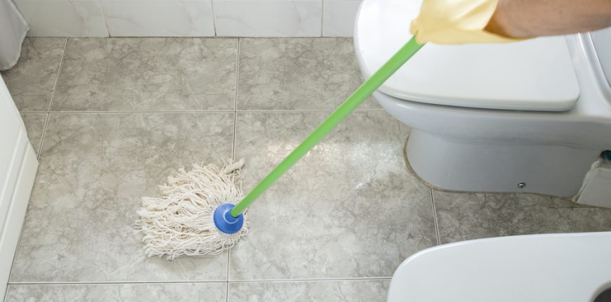Person wearing gloves cleaning the toilet floor with a mop